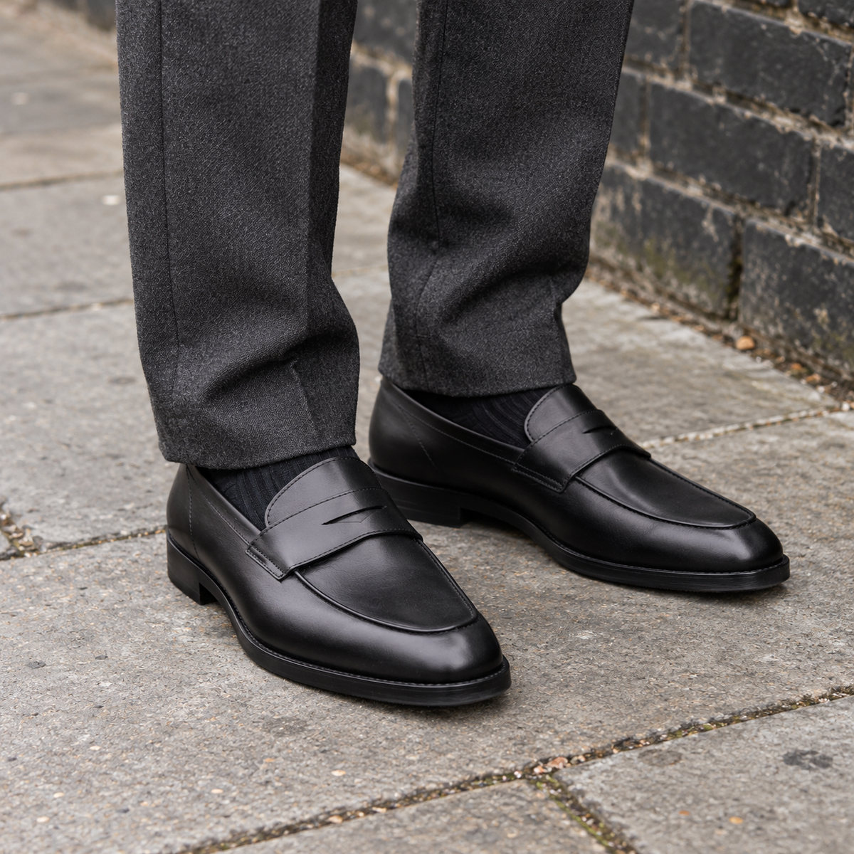 ASHFORD black calf leather penny loafers worn with charcoal trousers on a pavement